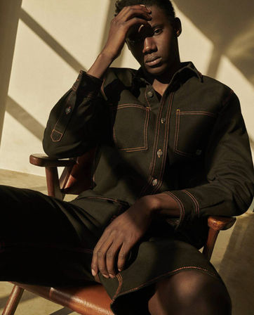 Man in olive shirt and shorts sits thoughtfully