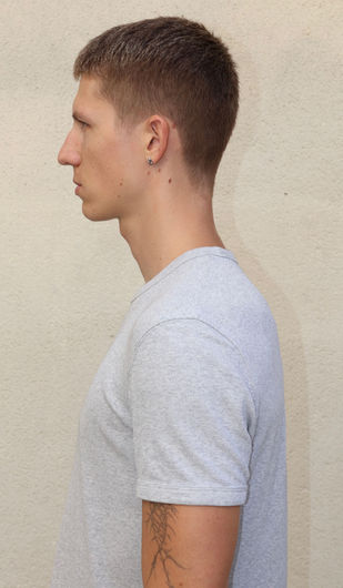 Young man's profile, short hair, gray t-shirt against plain background.
