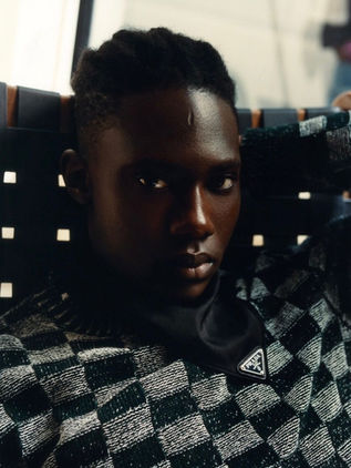 Dark-skinned french male model in black coat holding an elegant dark luxury handbag.