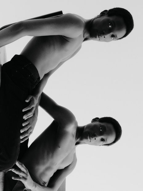 Black and white photo of The Twins, shirtless, sitting