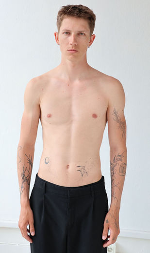 Model Elias with tattoos posing shirtless in black trousers