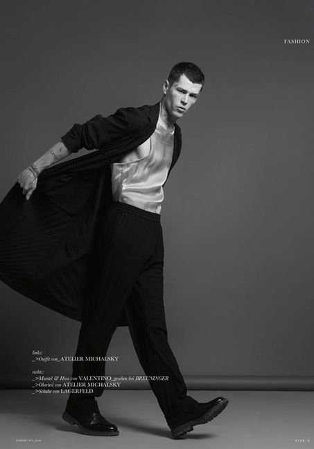 Norman Theuerkorn male model, three-quarter dark knitwear, neutral grey background, editorial tone