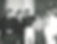 Five men pose indoors against a curtained backdrop. Three wear dark suits, one wears dark casualwear, and the other a white suit. Mood is calm.