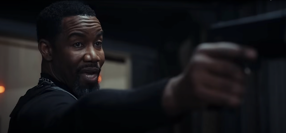 Man pointing a gun with a focused expression. Dimly lit room with dark colors, conveying tension. No visible text.