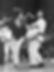 Two martial artists in white gis spar energetically in a crowded arena, with intense focus. Black belts are visible, capturing action mid-kick.