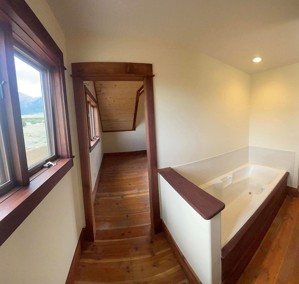 Bathroom with built-in tub, window, and hallway to stairs