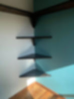 Three dark corner shelves on a light grey and blue wall.
