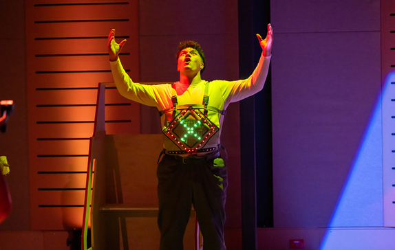 A man wearing an electronic panel on his chest raises his hands to the sky