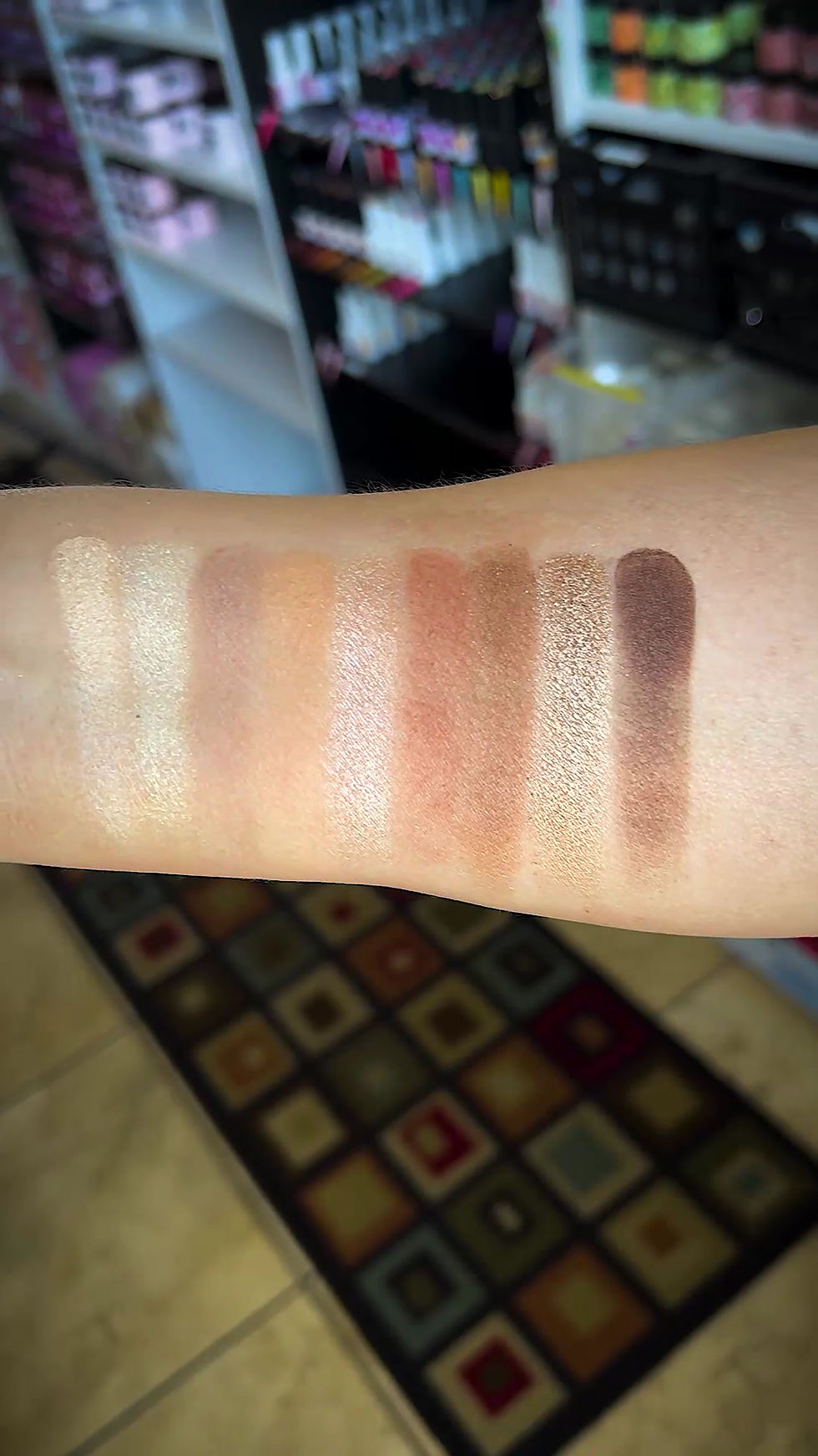 female hand holding an open xime beauty makeup pallet showing all nine colors; each color is also smeared on her forearm