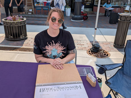 Owner of Lombard tattoo shop Bone & Blossom Sara, sitting at the chamber of commerce booth at the Lombard Farmers market in 2025