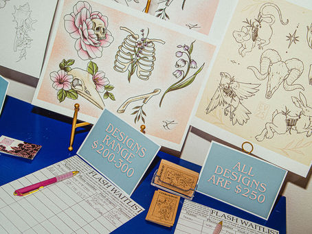 Tattoo designs on display, for Bone & Blossom Tattoo Studios Flash Event, featuring floral and skeletal motifs. Signs read "Designs Range $200-300" and "All Designs Are $250." A waitlist and pink pen are visible.