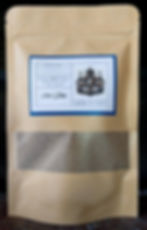 Un sac en papier contenant un mélange pour infusion, au fond duquel se trouve une fenêtre en film, permettant d'évaluer le contenu. En haut se trouve une étiquette dans un cadre bleu avec le nom de l'infusion.