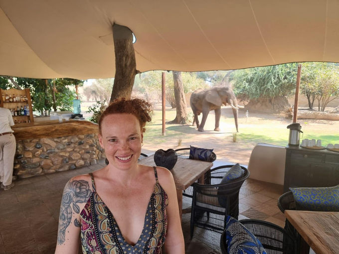 A woman at a Safari Camp in the Lower Zambezi Park smiling with an elephant behind her
