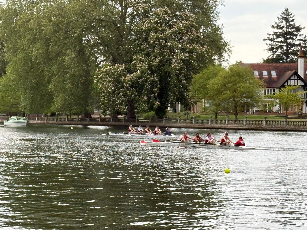 Two coxed rowing quads racing along a river with trees and a house in the background and a small motorboat parked in the background.