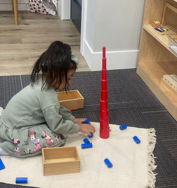 Little girl is working on building a tall tower with wooden toys.