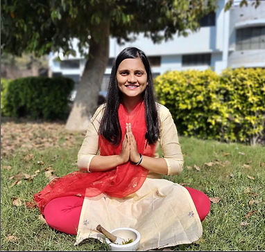 Omagen de namrata shahi en cruce simple de piernas y manos en postura de oración. Su vestimenta es tradicional de la india destacando los colores amarillo claro y rojo.