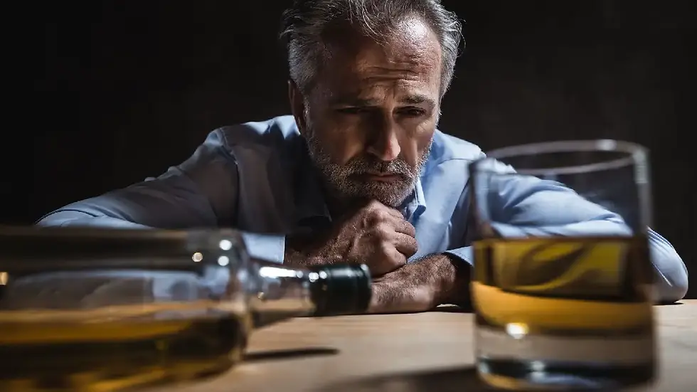 Mann sitzt nachdenklich vor einem Glas Alkohol und einer Flasche – Symbol für Alkoholabhängigkeit, inneren Schmerz und emotionale Überforderung