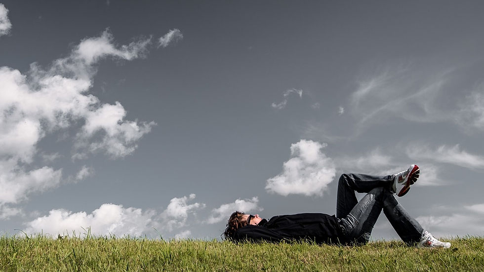 Person liegt entspannt im Gras unter wolkigem Himmel – Symbol für innere Ruhe und Achtsamkeit.
