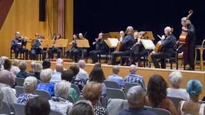 Kammerorchester spielt auf einer Bühne vor sitzendem Publikum in einem hellen Konzertsaal.