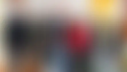 Sechs Personen posieren lächelnd vor einem Banner in einem Raum mit gelben Vorhängen. Eine Frau trägt ein rotes Jackett.