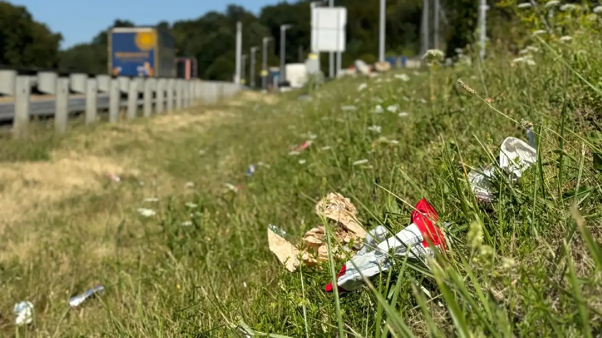 Papier und Plastikmüll neben einer Autobahn im Gras verstreut.