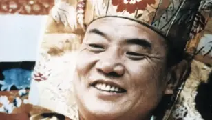 Nahaufnahme des lächelnden 16. Karmapa Rangjung Rigpe Dorje mit traditioneller Kopfbedeckung aus dem Dokumentarfilm „Meeting the Buddha“.