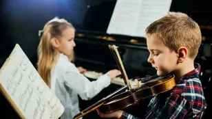 Kind spielt Violine, im Hintergrund begleitet ein weiteres Kind am Klavier.
