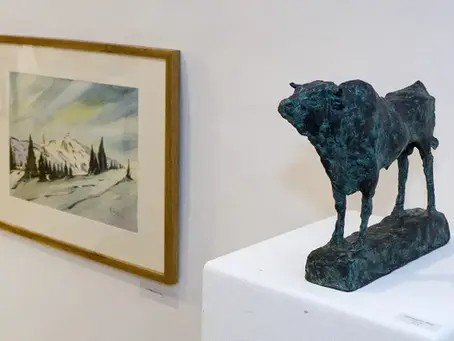 Galerie mit gerahmtem Winterlandschaftsbild und dunkler Rind-Skulptur auf weißem Podest.