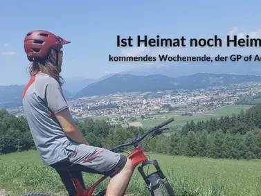 Radfahrer sitzt am Hügel und blickt auf das Murtal – im Hintergrund weite Landschaft und Vorbereitungen zur Formel 1, Symbol für stille Beobachtung und Wandel.