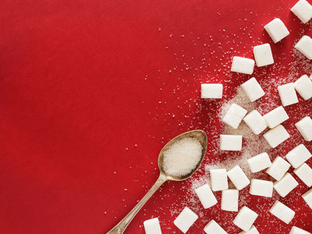Spoon with sugar and scattered sugar cubes on a vibrant red background. Sugar grains are sprinkled around, creating a dynamic pattern.
