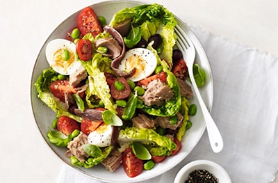 ohoto of tuna nicoise salad in a white bowel with fork