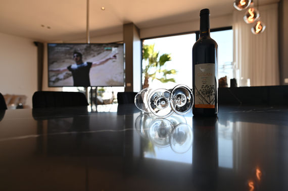 מבט מהאי המשוייש על הטלויזיה , בה רואים איש פורס את ידיו לצדדים , בקבוק יין על השיש ושתי כוסות