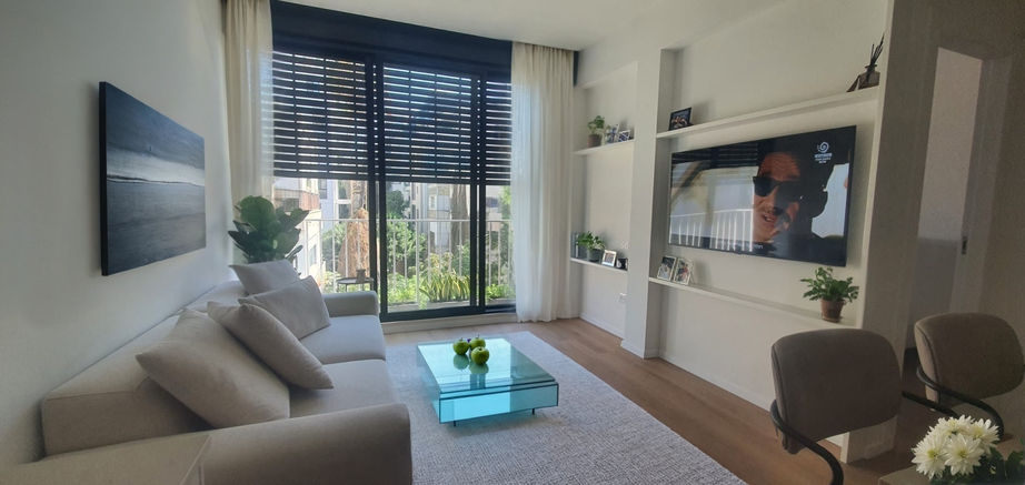 סלון בעיצוב מינימליסטי חמים בתל אביב – ספה בהירה, וילונות לבנים ואור טבעי רב