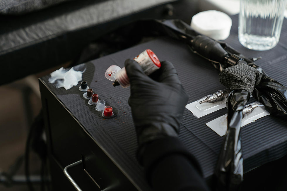 Close-up of gloved hands holding a tattoo machine, actively tattooing intricate line work on a person's forearm, which alread