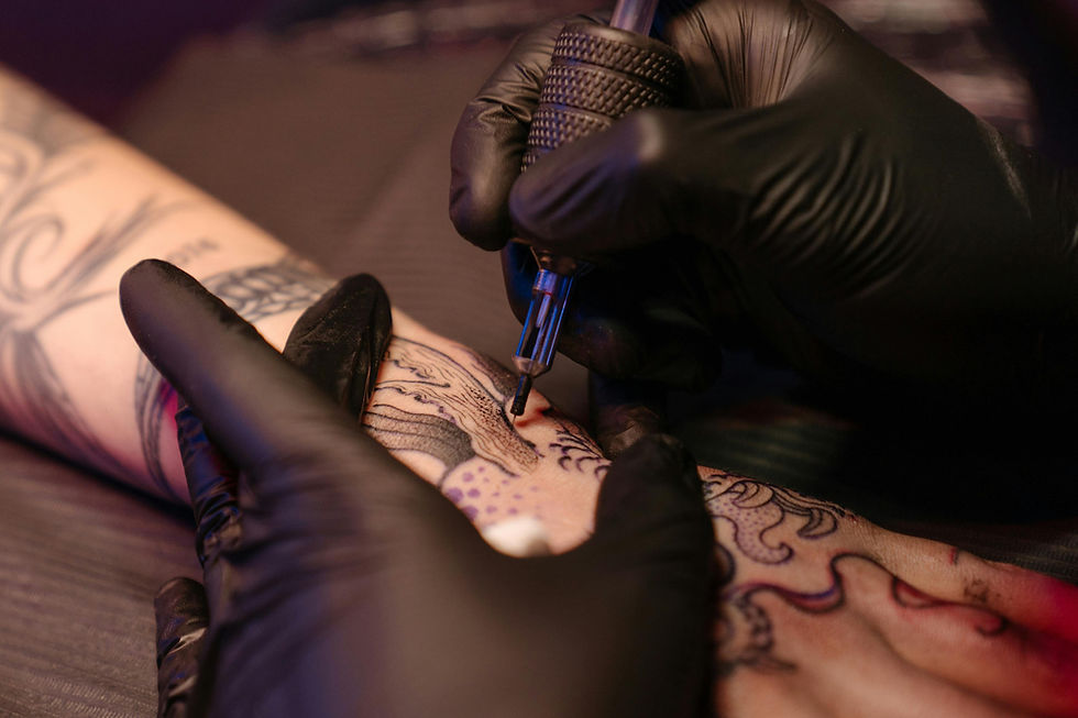 A gloved hand dispenses red tattoo ink into small cups on a black surface next to various tattoo needles and equipment.