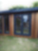 A garden room with a wooden exterior, dark-framed double doors, and large windows