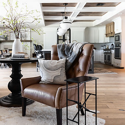 A cozy living space with a brown leather armchair adorned with a gray blanket and patterned pillow. A small side table stands