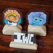Collectable coins artworks featuring 2 cartoon characters, a pirate and a robot, and vivid colors.   These artworks sits on a hand crafted wooden base made from eucalyptus wood. Created by IW Comics .Shop 