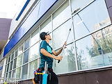An employee of a professional cleaning service in overalls washes the facade and windows w