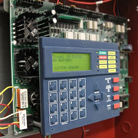 Close-up of a fire alarm control panel with wiring and display screen