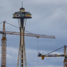 Seattle Space Needle with construction cranes in the foreground under a cloudy sky