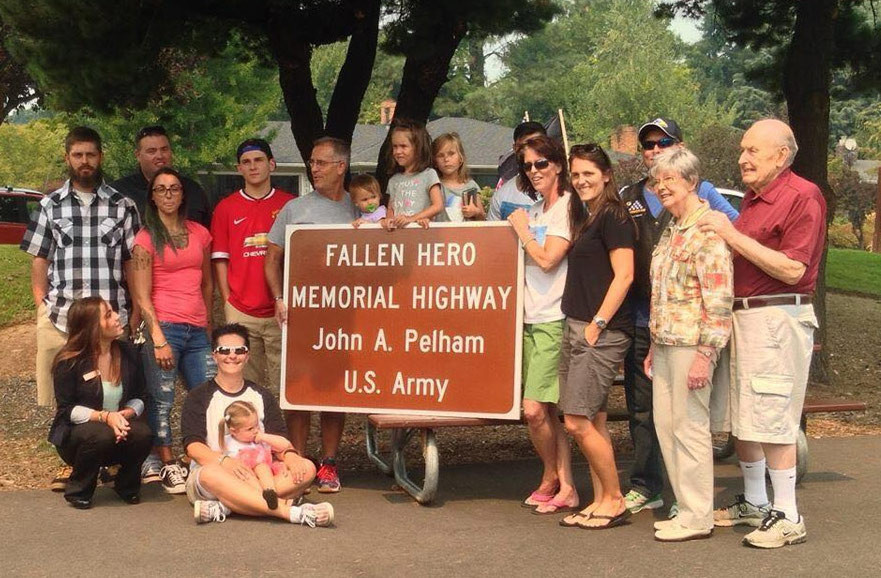 Group of people around highway sign for fallen hero
