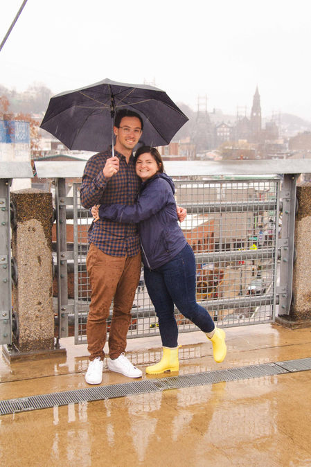 Portrait of a young couple in the rain. They stand on a bridge under the same umbrella, embracing and smiling for the camera