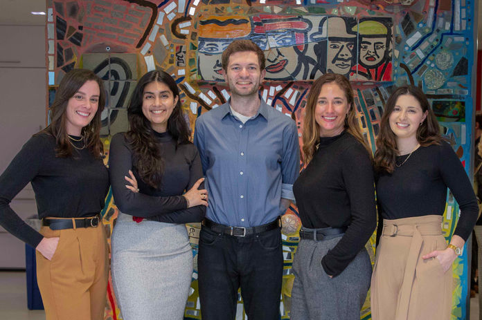 Portrait from an event. Five individuals stand together in an office, smiling at the camera