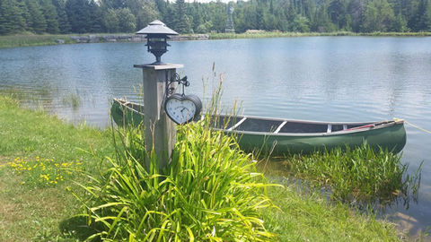 Green canoe by a lake with a lantern post and plants