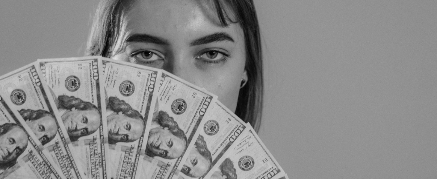 A woman holding a fan of hundered dollar bills. Photo by Tima Miroshnichenko.
