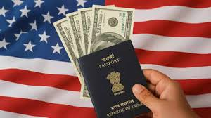 A hand holding an Indian passport and dollar bills in front of a United States flag, symbolizing the process and economic aspects of obtaining a US visa.