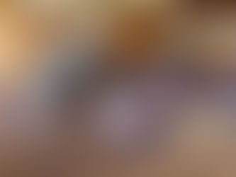 A yoga instructor helps a woman in a restorative pose on a purple mat in a wooden-floored studio. Participants observe in the background, creating a focused and calm atmosphere.