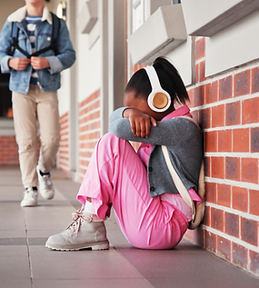 Little girl sitting with head on knees, wearing backpack