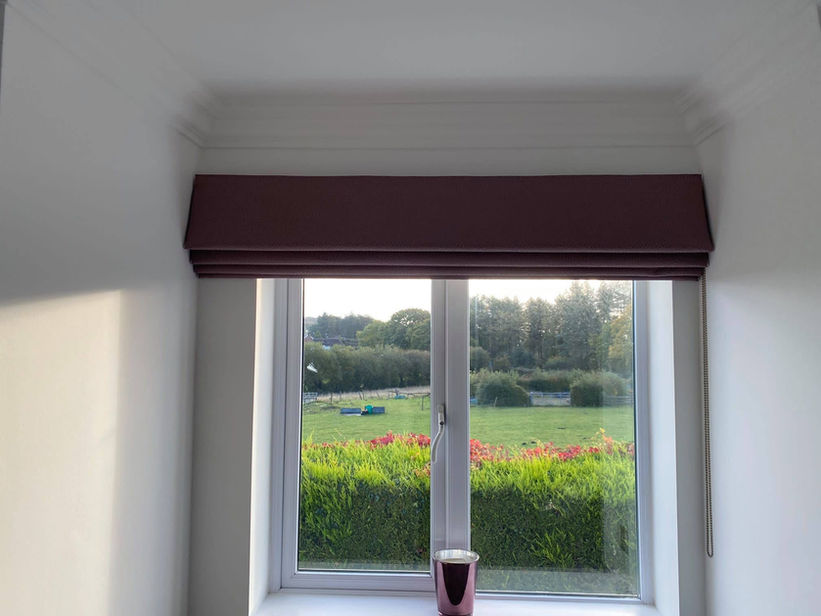 plum coloured Roman blind at small window framing view of pretty garden